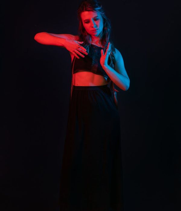 Woman performing a graceful yoga pose in a dark studio with crimson light.